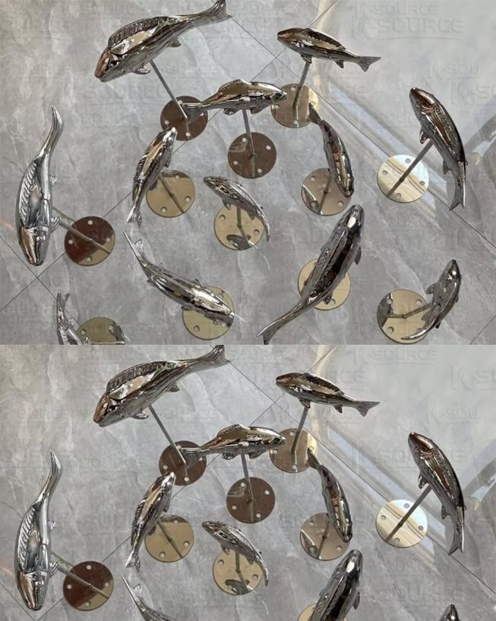 A stainless steel sculpture surrounded by a group of small fishes
